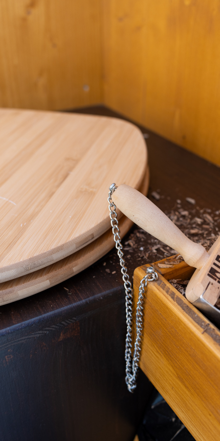 Bild vom Innern eines Kompotois mit Blick auf dengeschlossenen WC-Deckel aus Holz sowie auf die Holzschnitzel zum Streuen nach dem Geschäft. 