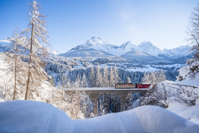 Die Rhätische Bahn in der Winterlandschaft der Ferienregion Engadin Scuol Zernez – Schloss Tarasp im Hintergrund – Dominik Täuber Die Rhätische Bahn in der Winterlandschaft der Ferienregion Engadin Scuol Zernez – Schloss Tarasp im Hintergrund – Dominik Täuber