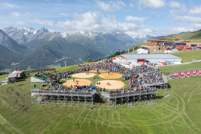 Blick auf das Schwingfestgelände in Scuol mit Arena, Publikum und umliegender Berglandschaft.