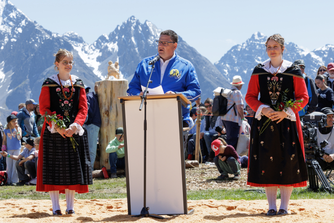 Eröffnungsrede am Schwingfest in Scuol mit Trachtenträgerinnen vor alpiner Bergkulisse.