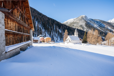 Winter in S-charl im Unterengadin – idyllisches Bergdorf mit Kirche, Holzhäusern und verschneiter Alpenkulisse in Graubünden